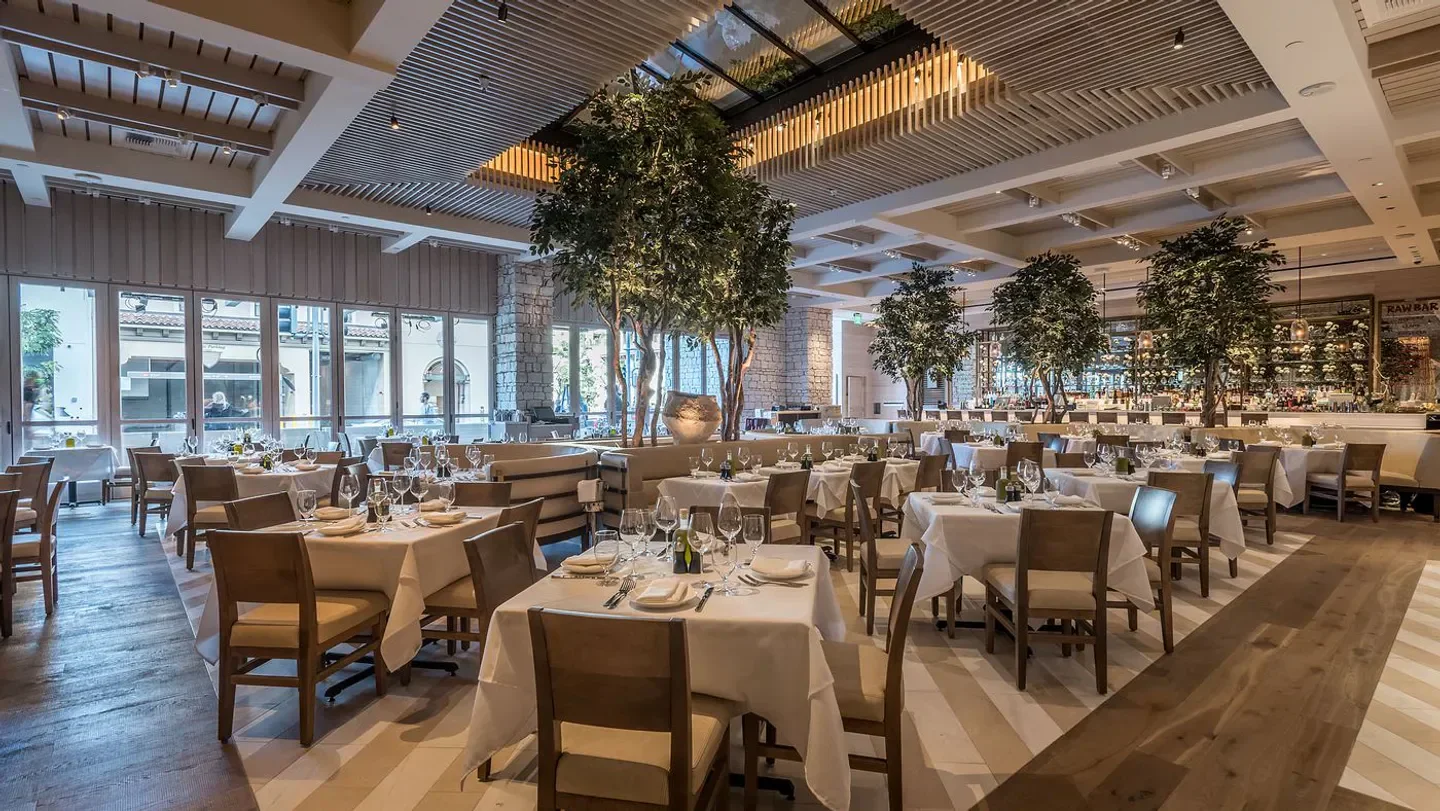 Elegant dining room at Avra in Los Angeles, featuring lush greenery and stylish tables