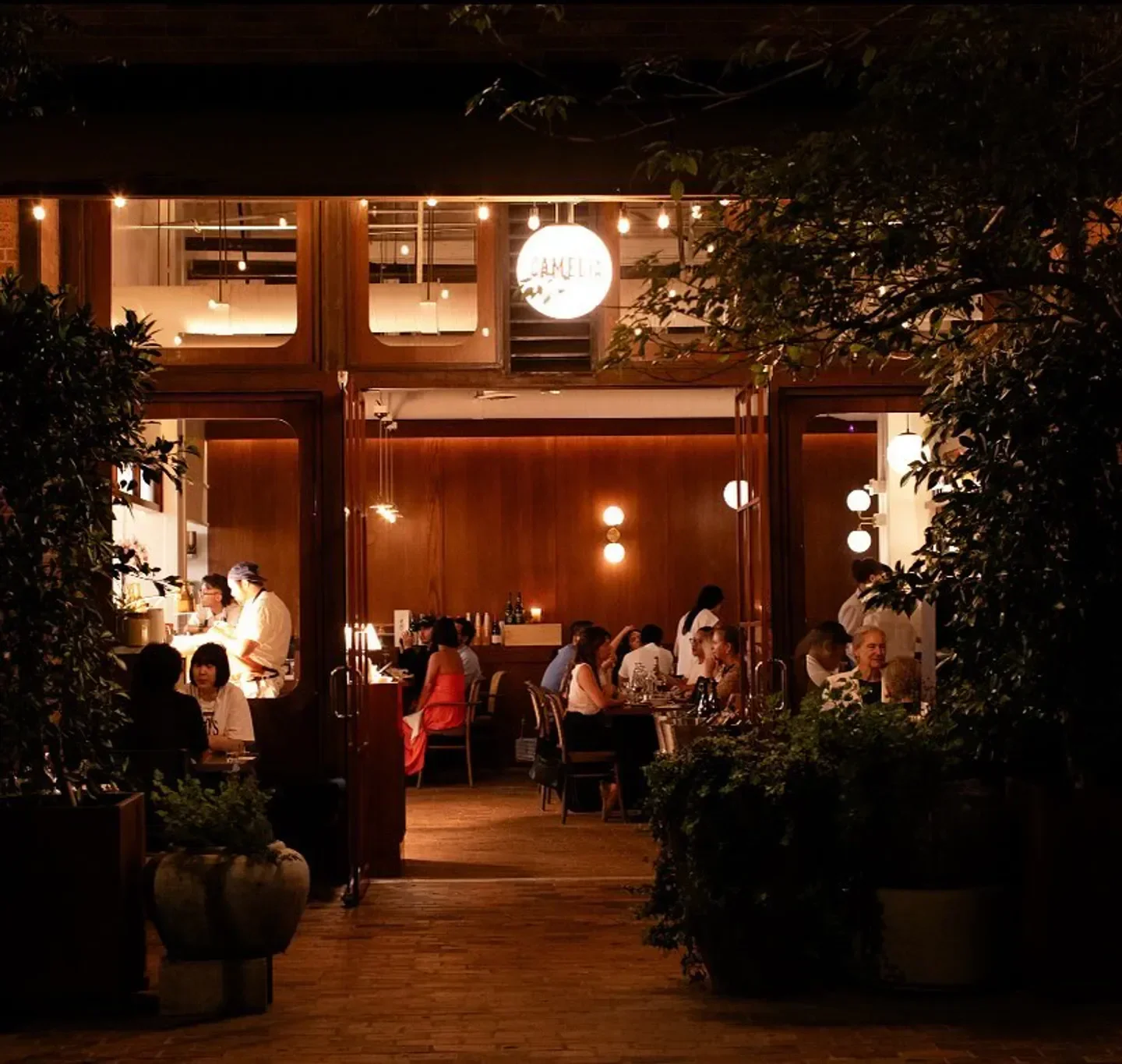 Exterior view of Camélia restaurant in Los Angeles at night, with diners visible