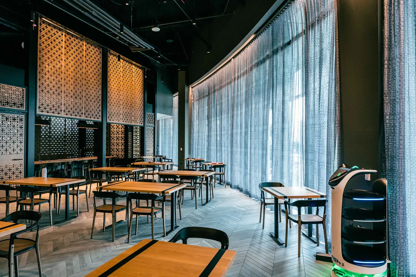 Interior of NIKU X in Los Angeles with tables, chairs, and decorative window panels.