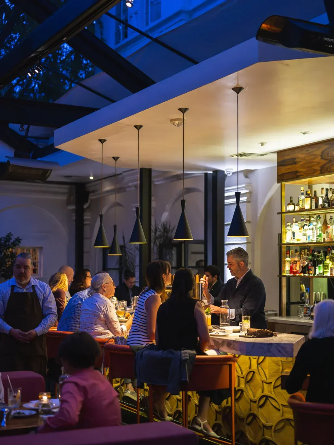 Stylish interior of Redbird restaurant in Los Angeles, bar with customers and server.