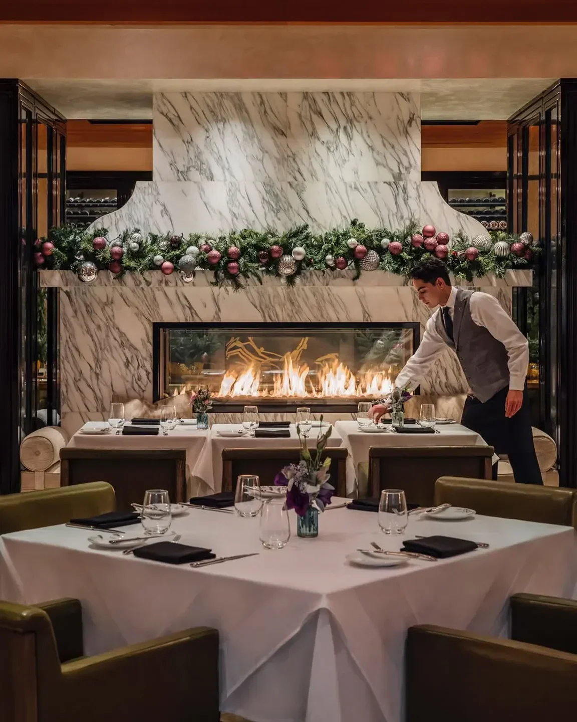 Waiter setting table at The Restaurant at Hotel Bel-Air in Los Angeles, fireplace view